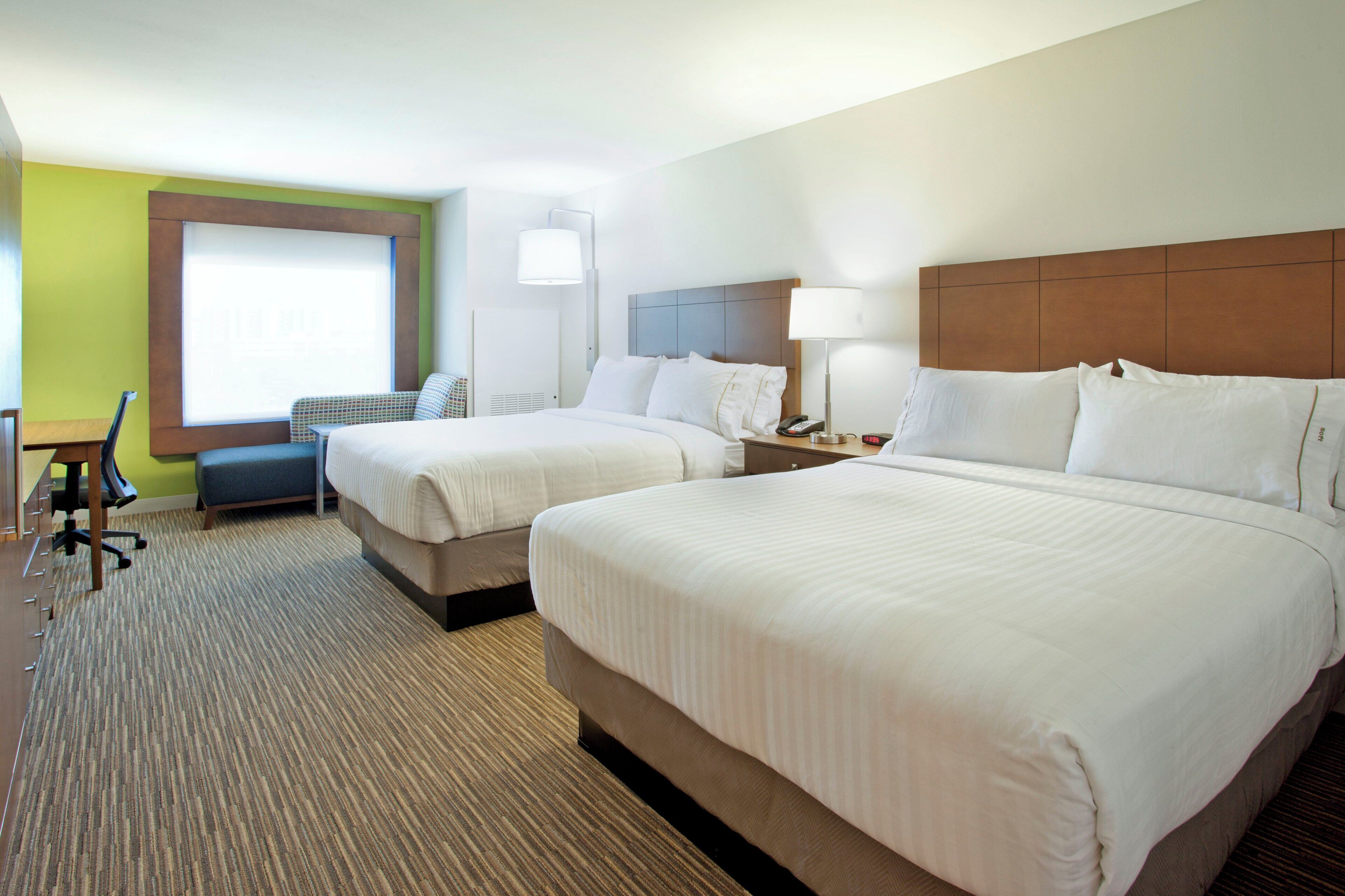A hotel room with two beds, a desk, a chair, a lamp, and a window.