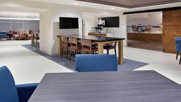 Un espace repas moderne comprenant une grande table et des chaises, un coin cuisine avec un comptoir, et un coin salon avec des canapés et des fauteuils.