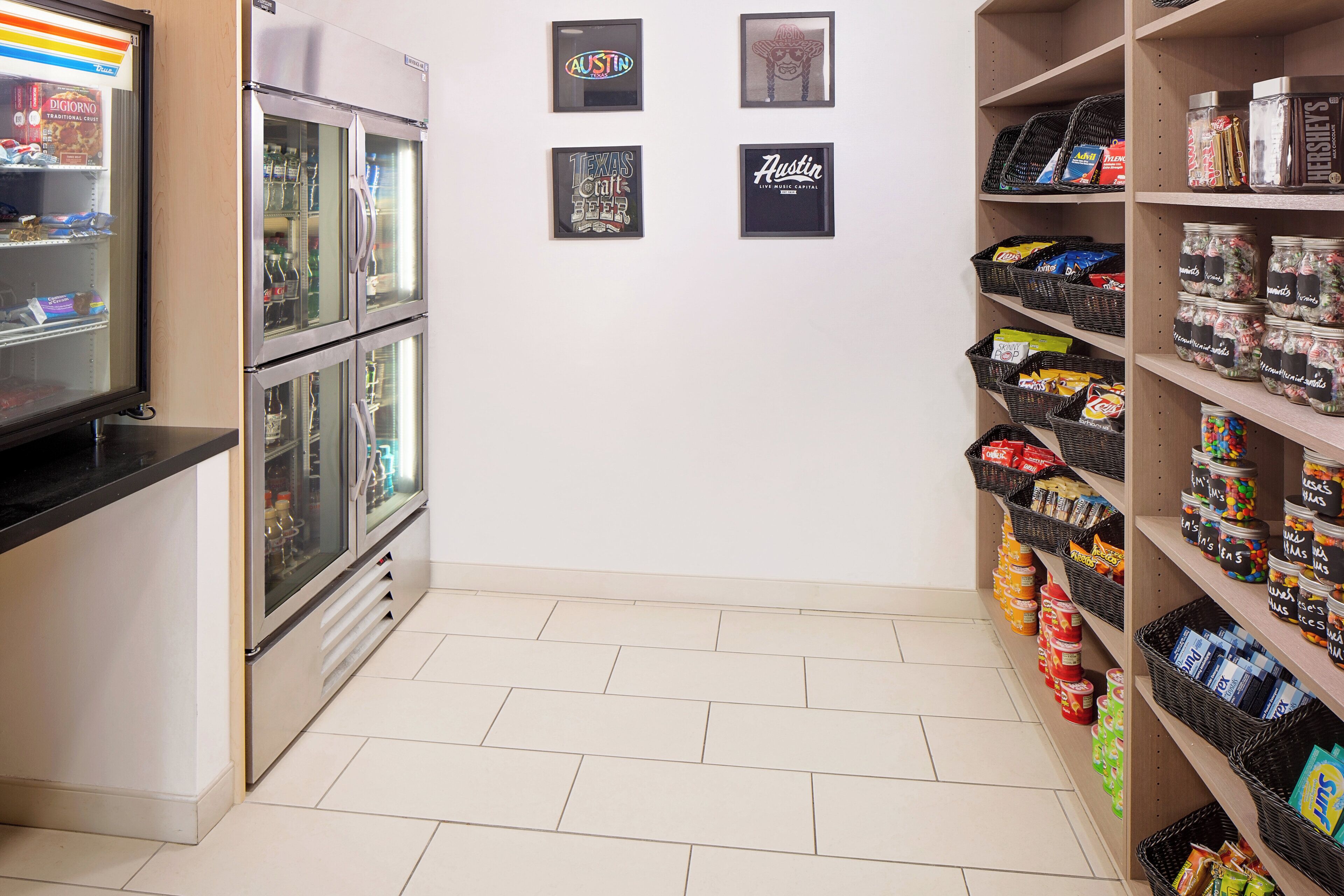 Zona de aperitivos y bebidas con refrigeradores, estantes llenos de tentempiés y carteles enmarcados en la pared.
