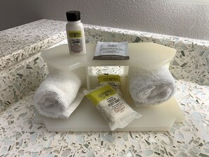 Un meuble-lavabo de salle de bain avec des articles de toilette, notamment un flacon de lotion, un savon et deux serviettes.