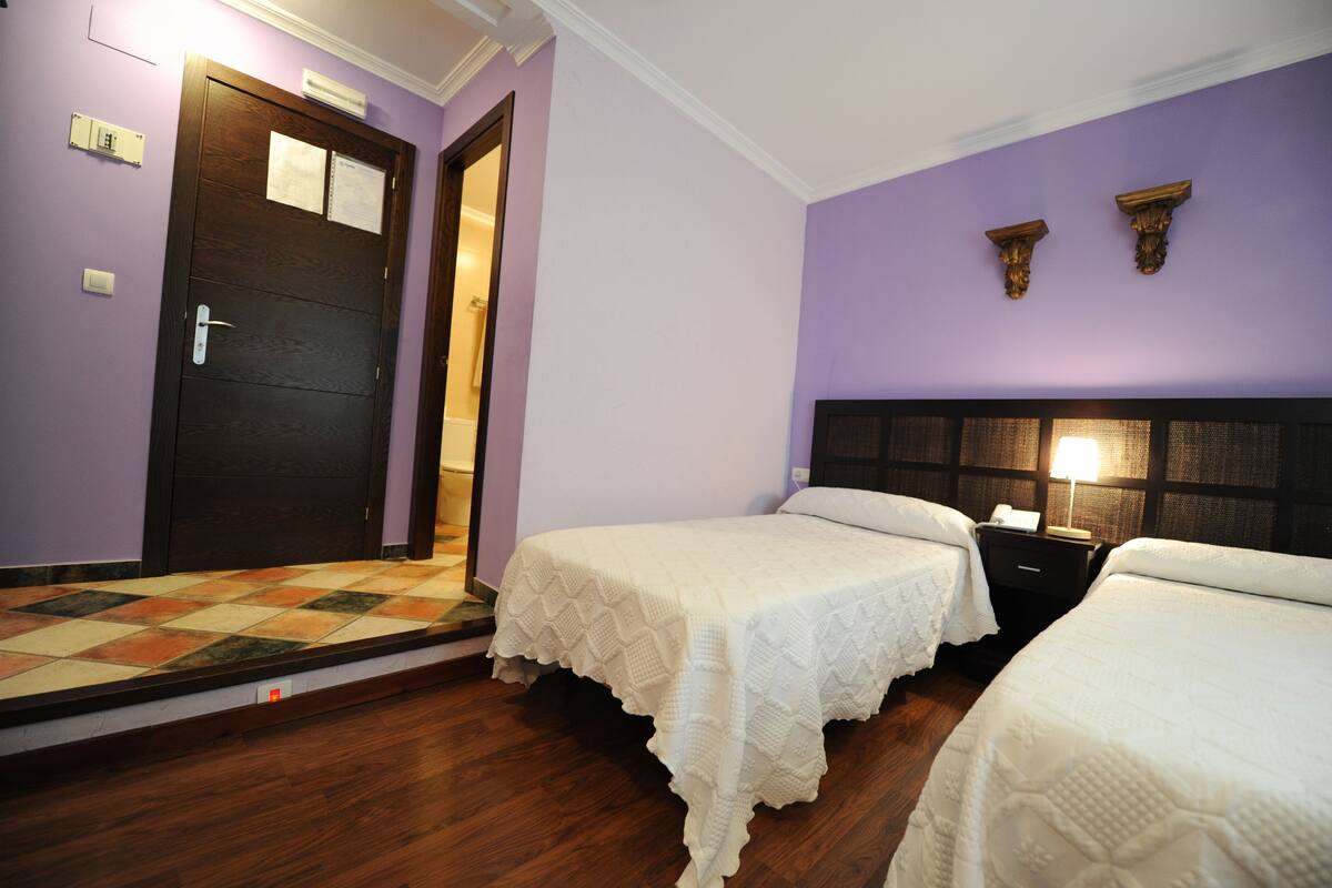 Een hotelkamer met twee bedden, een houten vloer, een paarse muur en een deur met een lamp erboven.