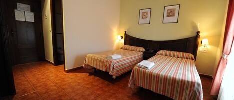 Habitación de hotel con dos camas individuales, una puerta de madera y suelo de baldosas.