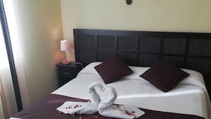 A neatly made bed with a dark headboard, two wall-mounted sconces, and a decorative swan towel arrangement on the bed.