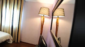 Quarto de hotel com cama, cortinas, luminária de chão e espelho refletindo a luminária.