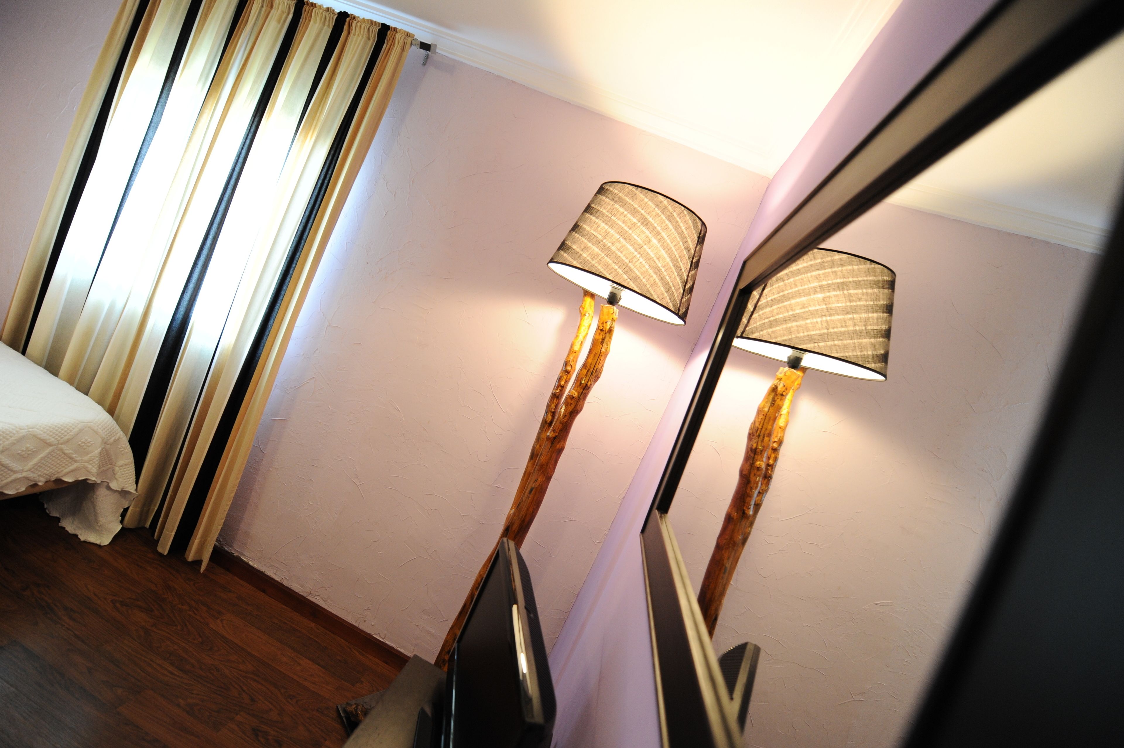 A room with a bed, two standing lamps, and a mirror reflecting the lamps.