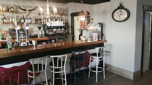 A bar area with a long counter, multiple stools, a coffee machine, and a clock on the wall. - Hotel Montearoma (Valverde del Camino)