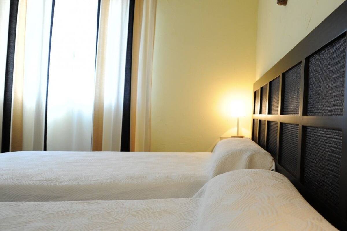 Een hotelkamer met twee bedden, een groot raam met gordijnen en een wand met een gestructureerd paneelontwerp.