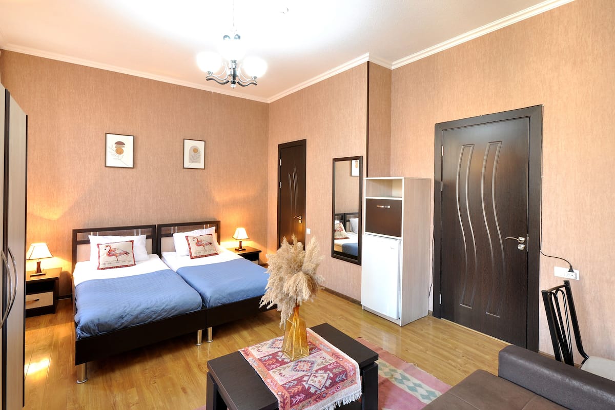 A hotel room with a double bed, bedside lamps, a small table with a vase, a mirror, and a wardrobe.