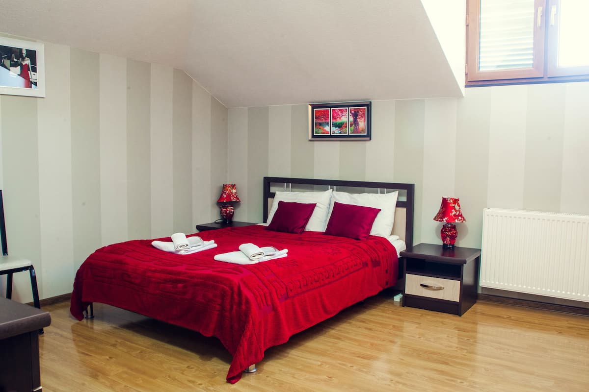 A neatly made bed with red bedding, a bedside table with a lamp, and a framed picture on the wall.