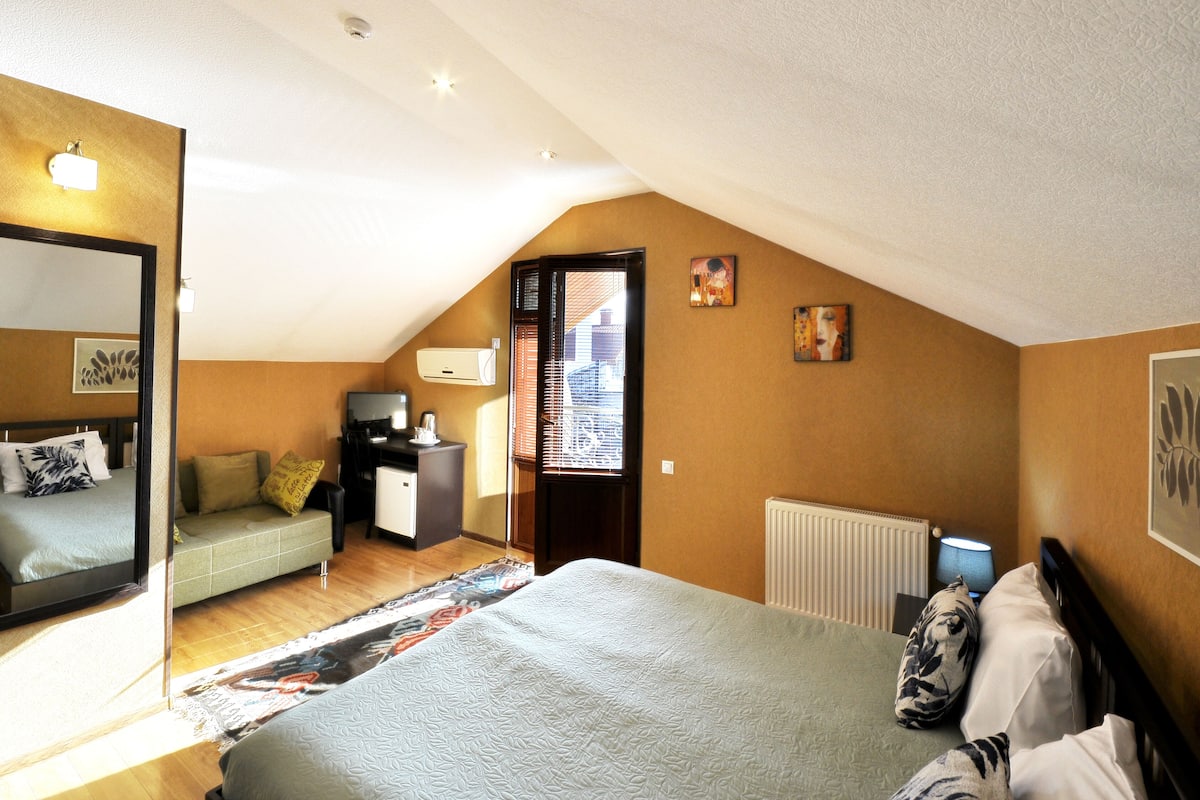 A bedroom with a bed, a sofa, a desk, and a window with blinds.