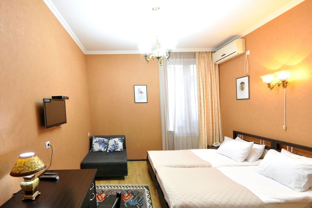 A hotel room with a bed, a sofa, a desk with a lamp, a TV, and a chandelier.