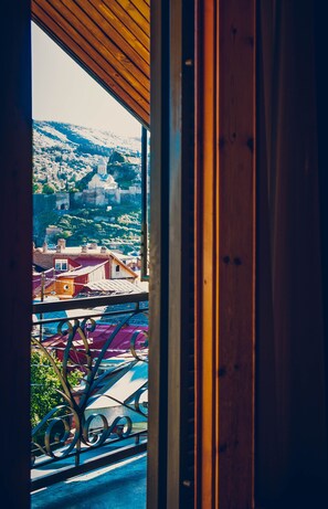 Vista desde un balcón con baranda de madera, sobre un pueblo con edificios y una colina al fondo.
