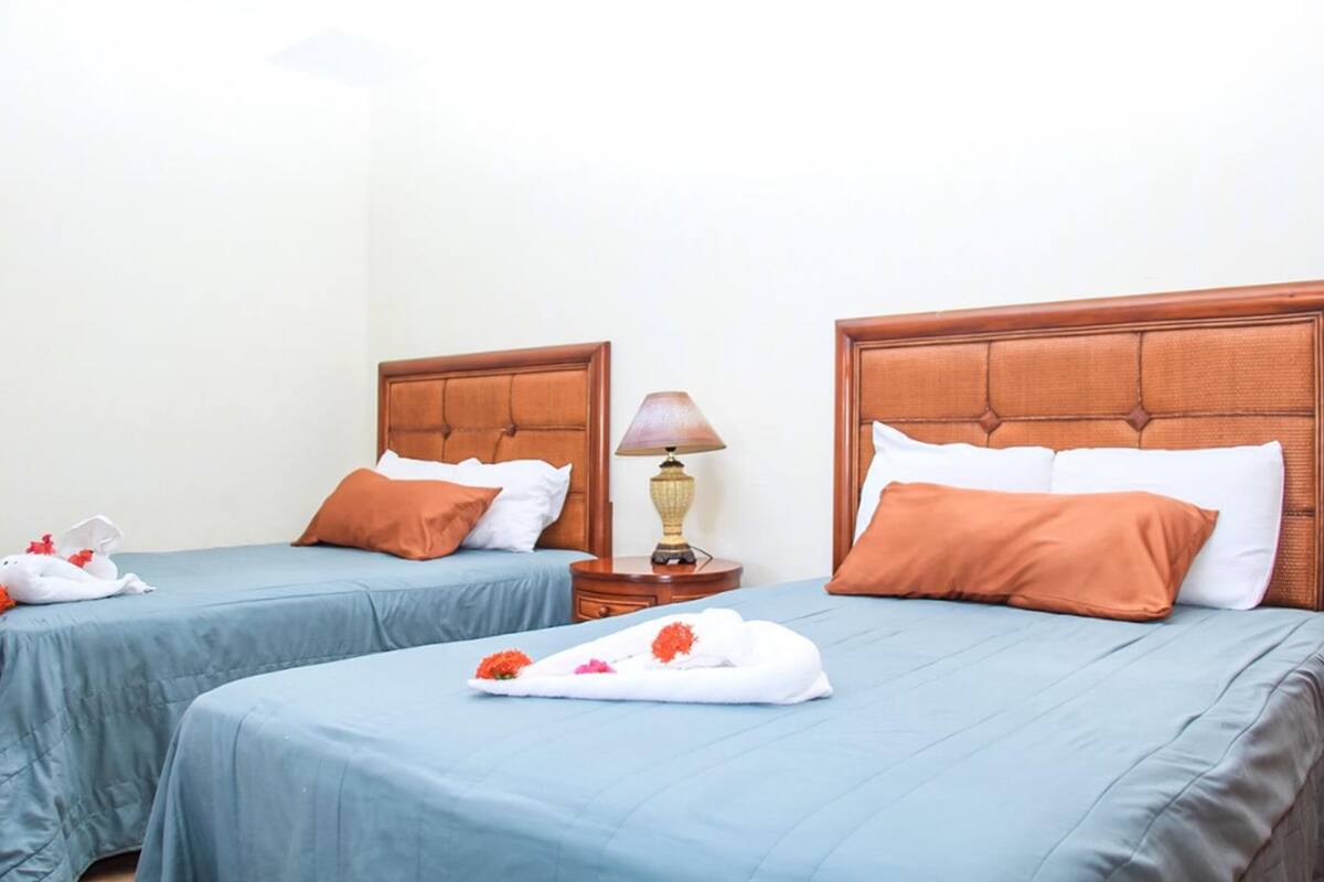Two twin beds with wooden headboards, a bedside table with a lamp, and a tray with flowers on the larger bed.