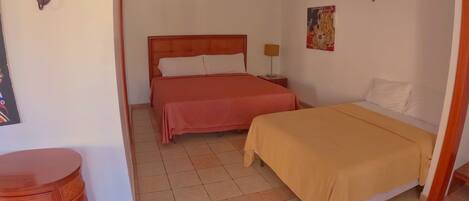 Habitación de hotel con dos camas, cabecera de madera, una mesita y aire acondicionado instalado en la pared.