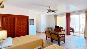 Une chambre d’hôtel avec deux lits, un ventilateur de plafond, une télévision et un balcon avec des rideaux.