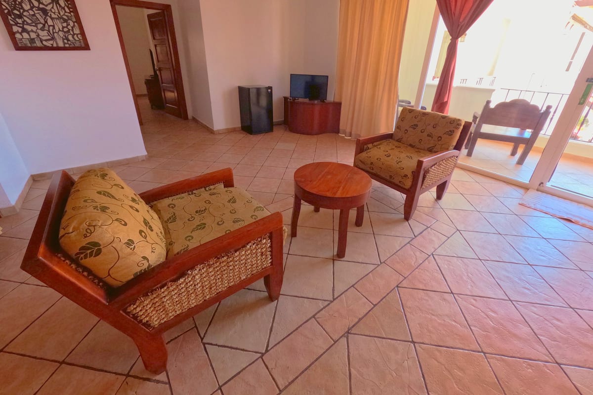 A living room with a sofa, armchair, and round table, a television, and a small cabinet.