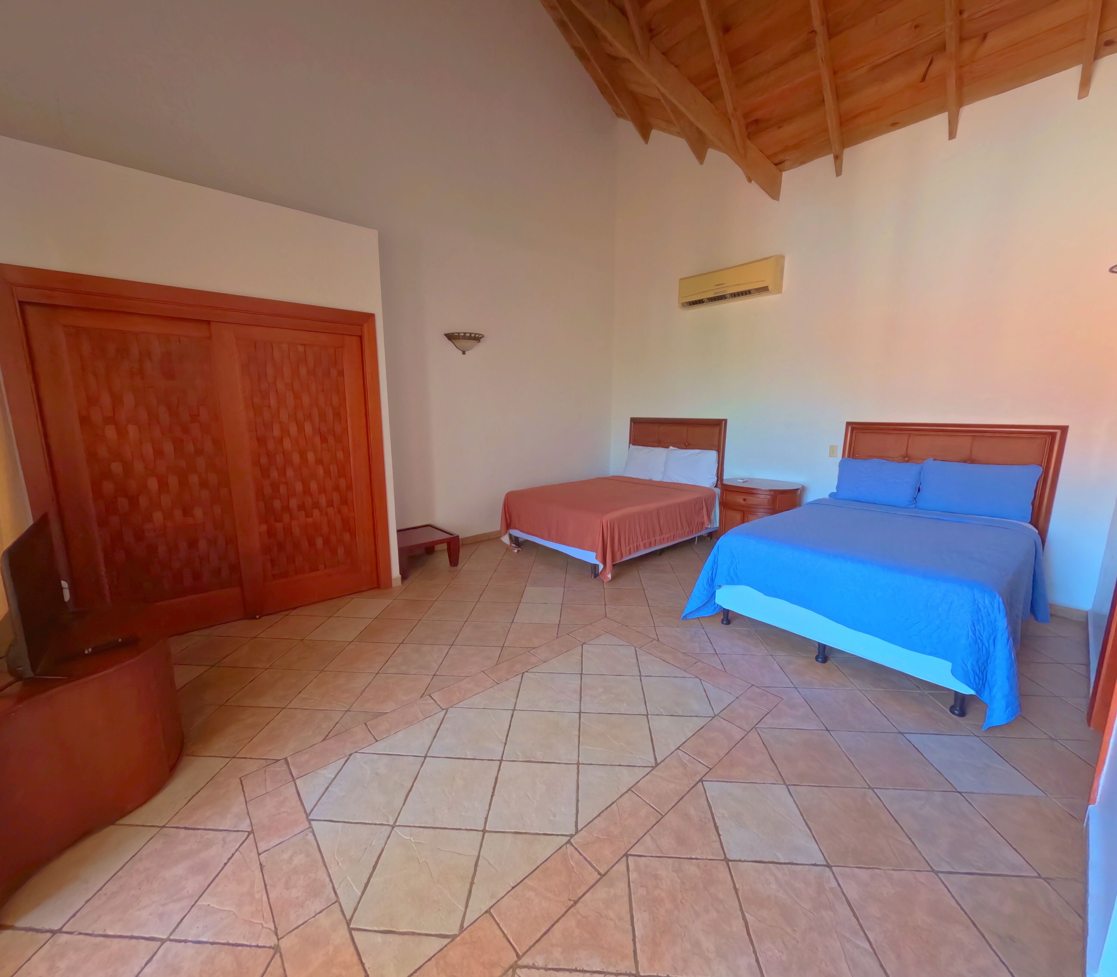 Habitación de hotel con dos camas, un armario de madera, una mesita pequeña y suelo de baldosas.