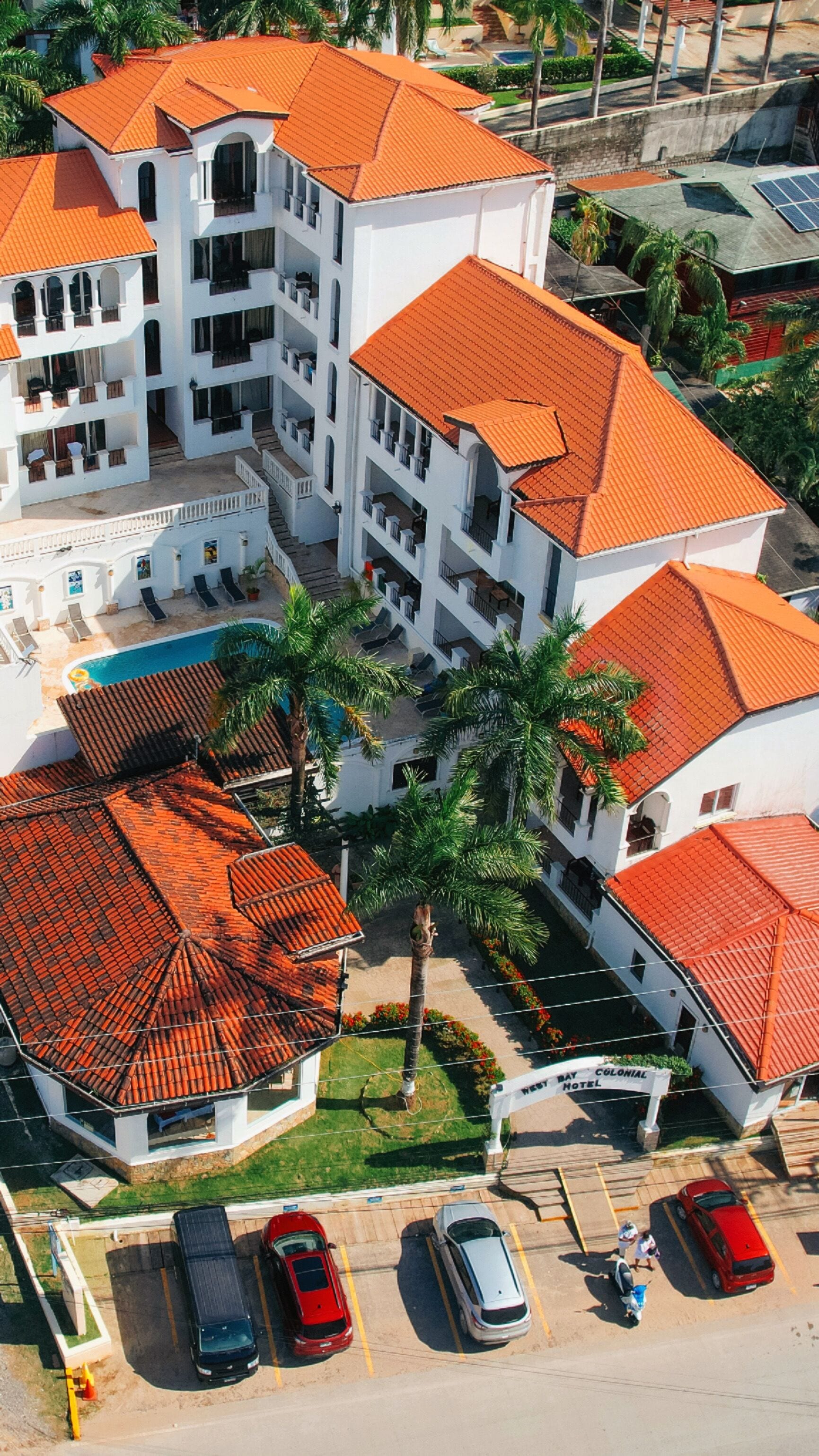 Un hôtel à plusieurs étages doté d’une piscine, de palmiers et d’un toit recouvert de tuiles rouges.