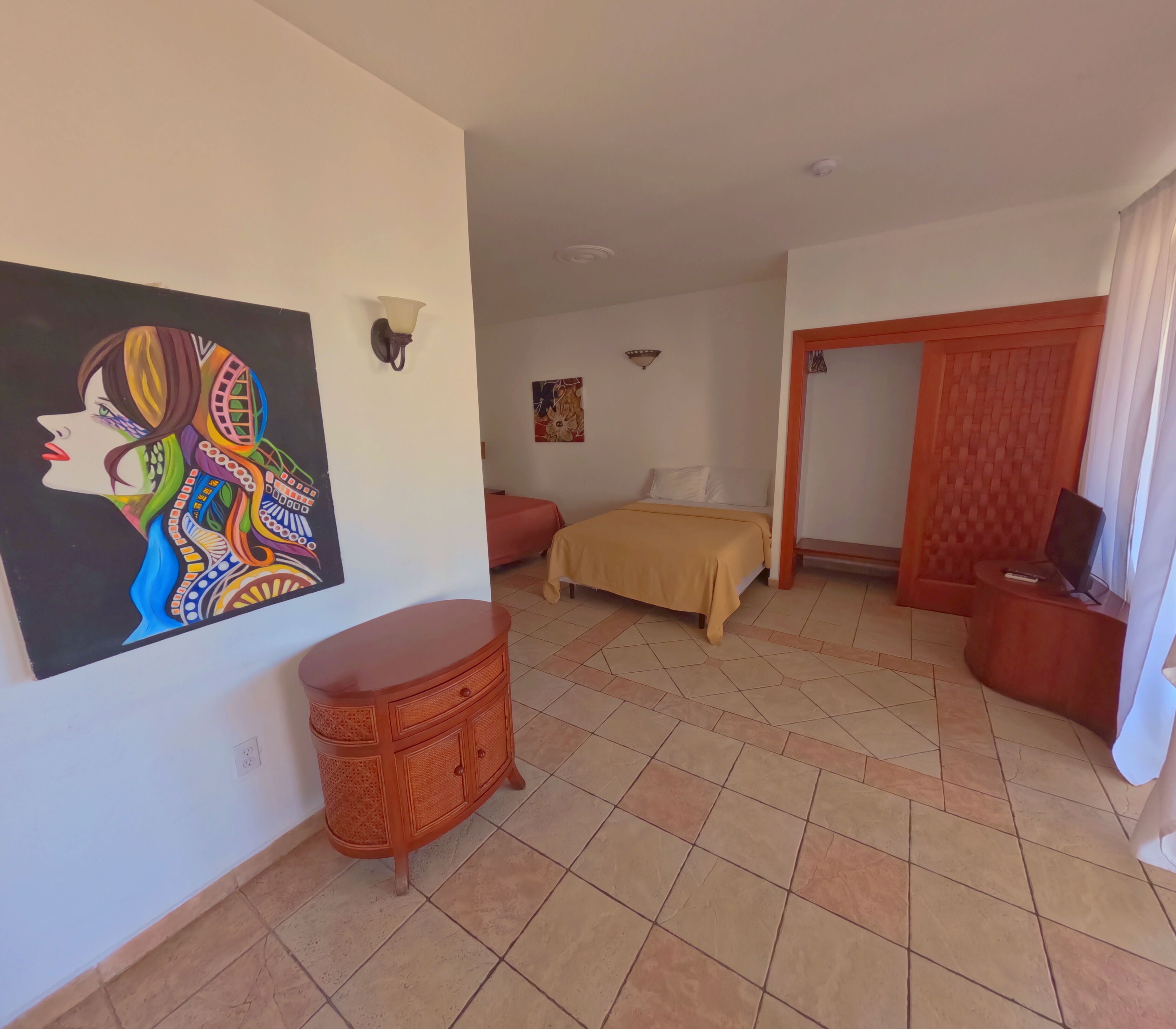 Habitación de hotel con cama, mesita de madera, lámpara de pared y un cuadro.