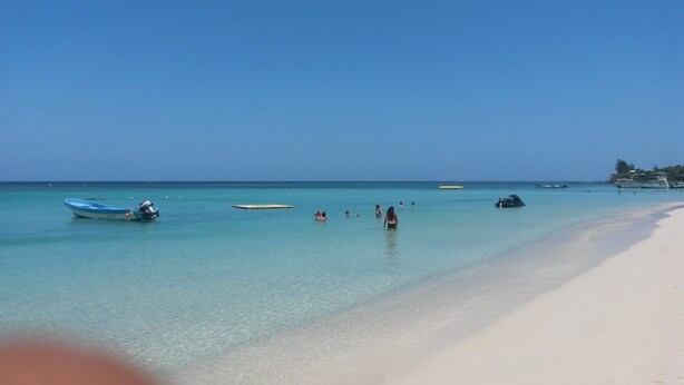 Une plage à l’eau turquoise et limpide, un rivage sablonneux et plusieurs bateaux.