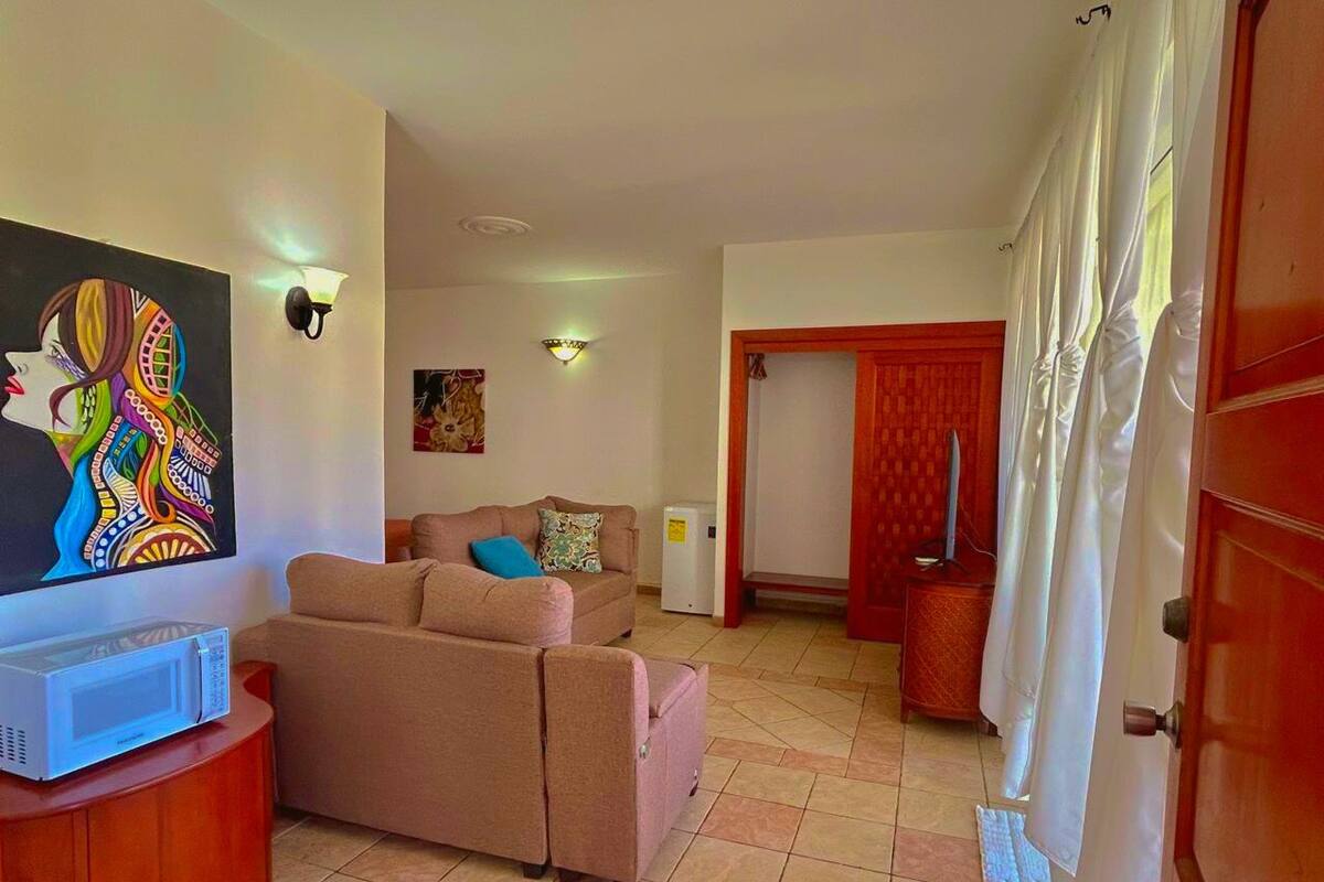 A living room with a sofa, a television, and a microwave on a wooden cabinet.