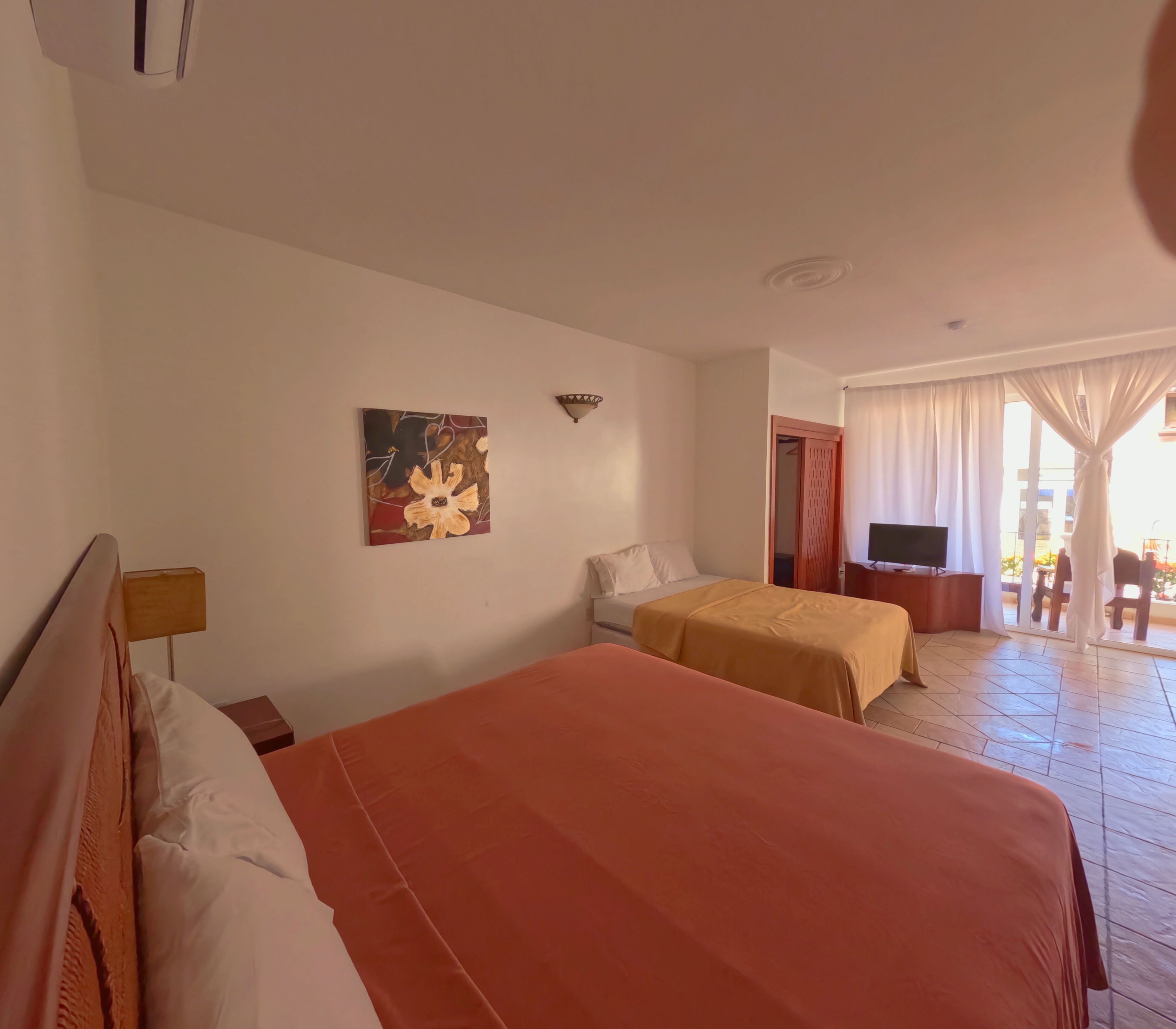 Habitación de hotel con dos camas, un cuadro en la pared, un televisor y un balcón con cortinas.