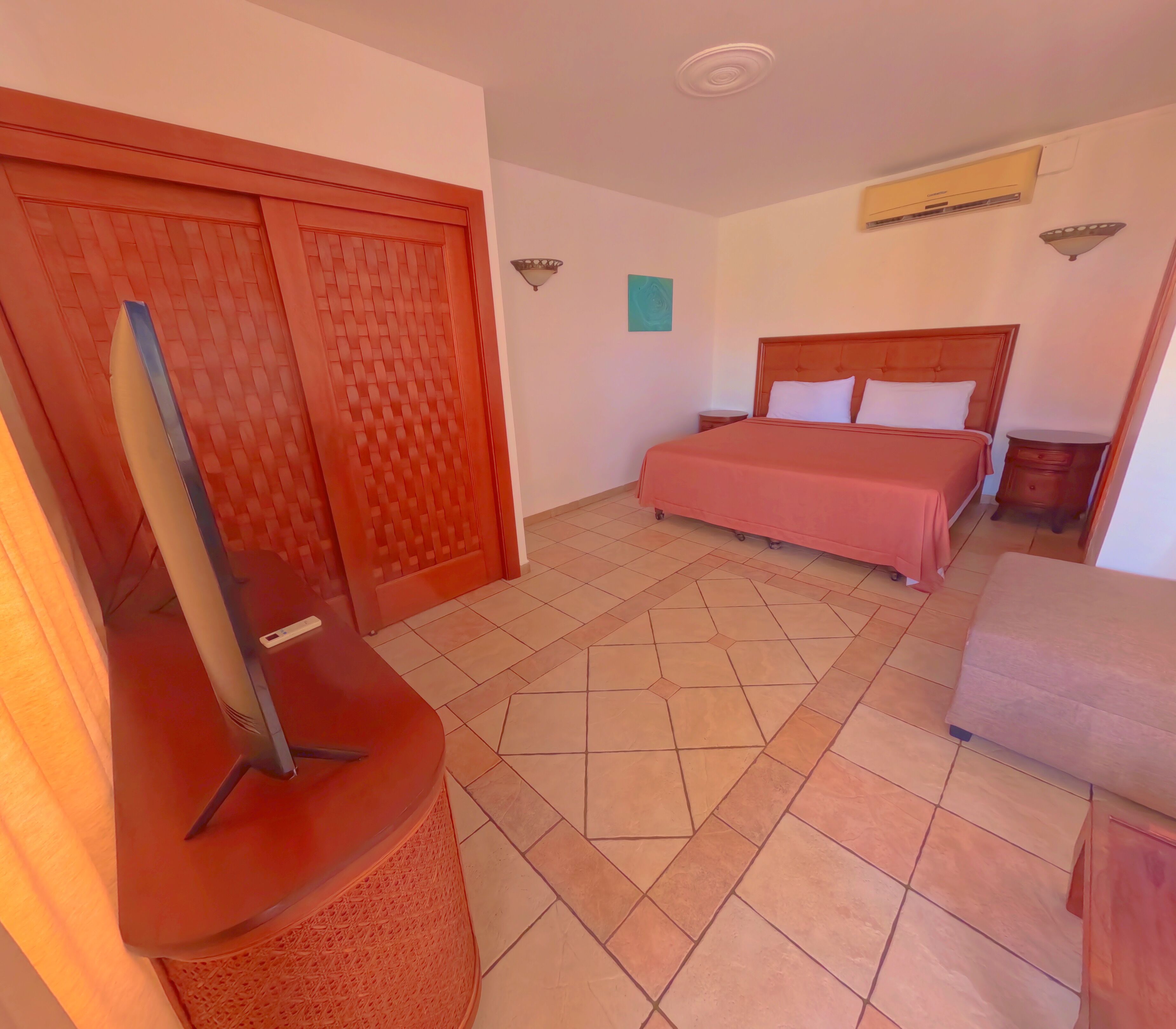 A hotel room with a bed, a TV, a wardrobe, and a small table.