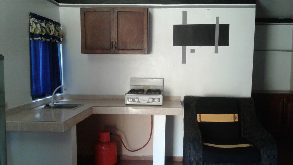 Una cocina pequeña con estufa a gas, un lavamanos y un cilindro de gas rojo.