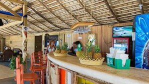 Un restaurante con techo de paja, barra de madera y sillas color naranja.