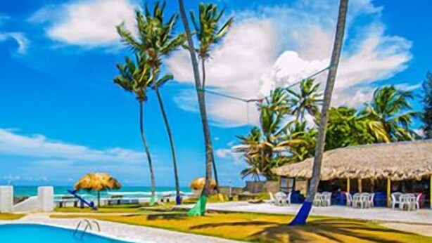 Una piscina con cielo azul despejado, palmeras y una playa al fondo.