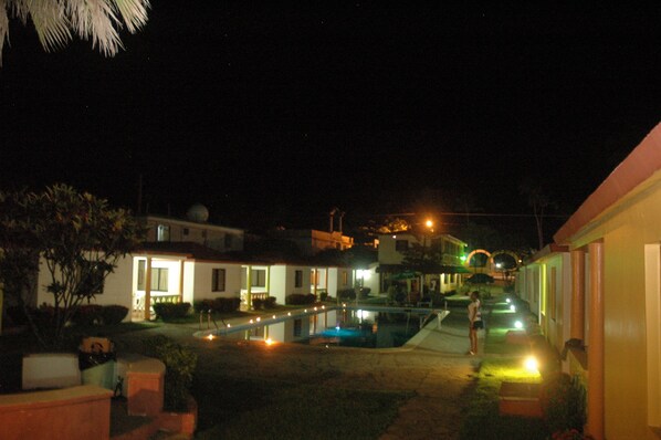 A nighttime view of a residential area with houses, a swimming pool, and a person standing by the pool.