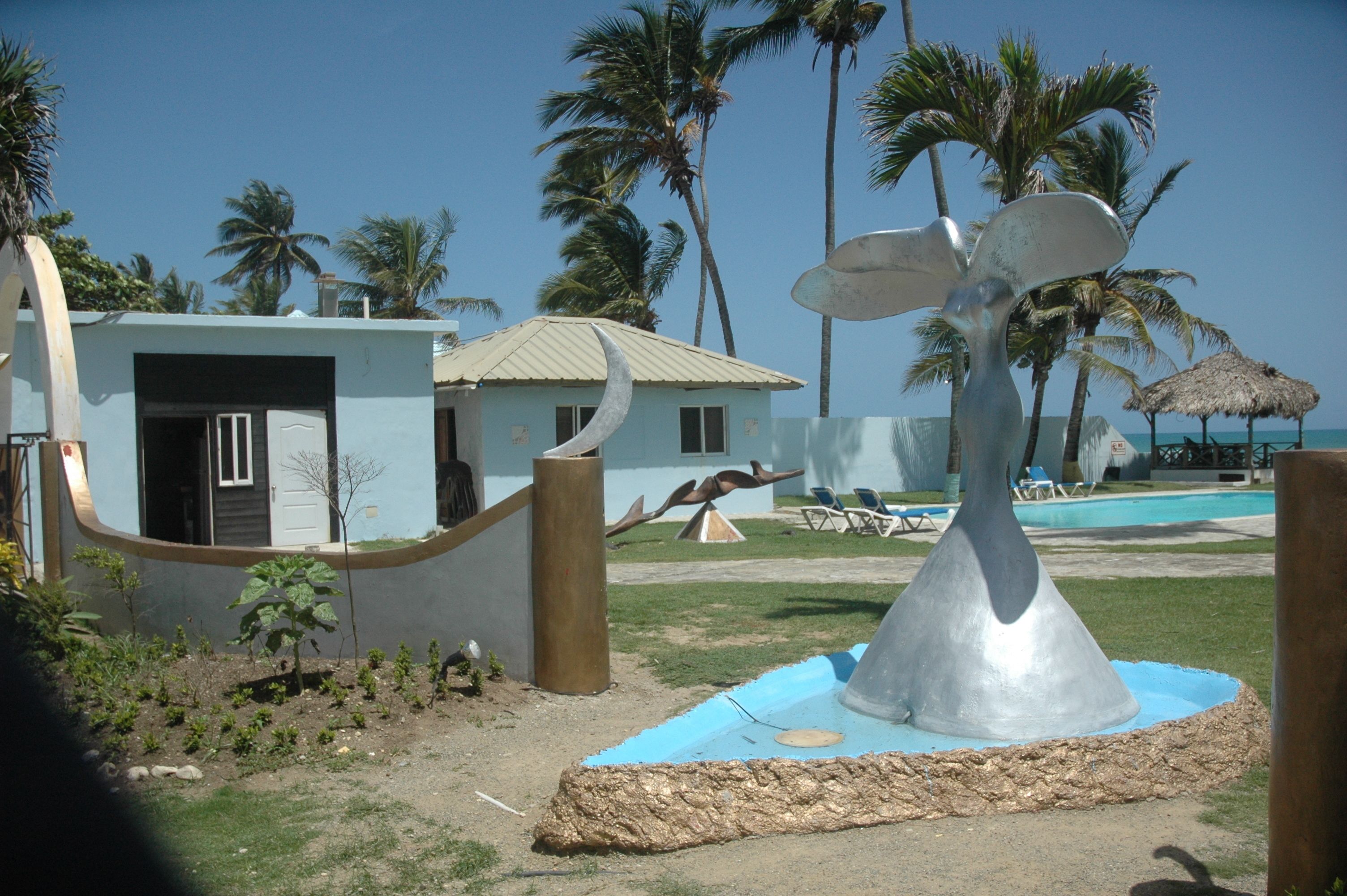 A pool area with a unique sculpture, palm trees, and a small building with a thatched roof.