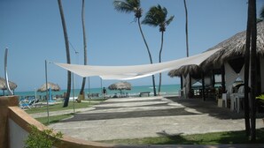 Un resort frente a la playa con estructuras de techo de paja, sillas de descanso y una vista despejada del océano.