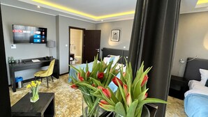 Una habitación de hotel con una cama, un escritorio, un televisor y un jarrón con flores.