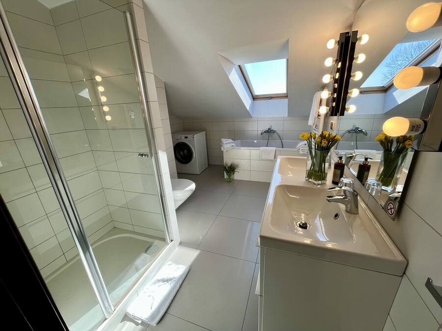 Ein modernes Badezimmer mit Duschkabine aus Glas, integriertem Waschmaschinenanschluss, Badewanne und Waschtisch mit Spiegel.