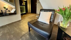 Habitación de hotel moderna con sofá de cuero negro, almohada blanca, florero de vidrio con flores y un espejo que refleja la habitación.