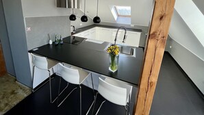 Una cocina moderna con encimera negra, sillas blancas, pileta de acero inoxidable y tragaluz.