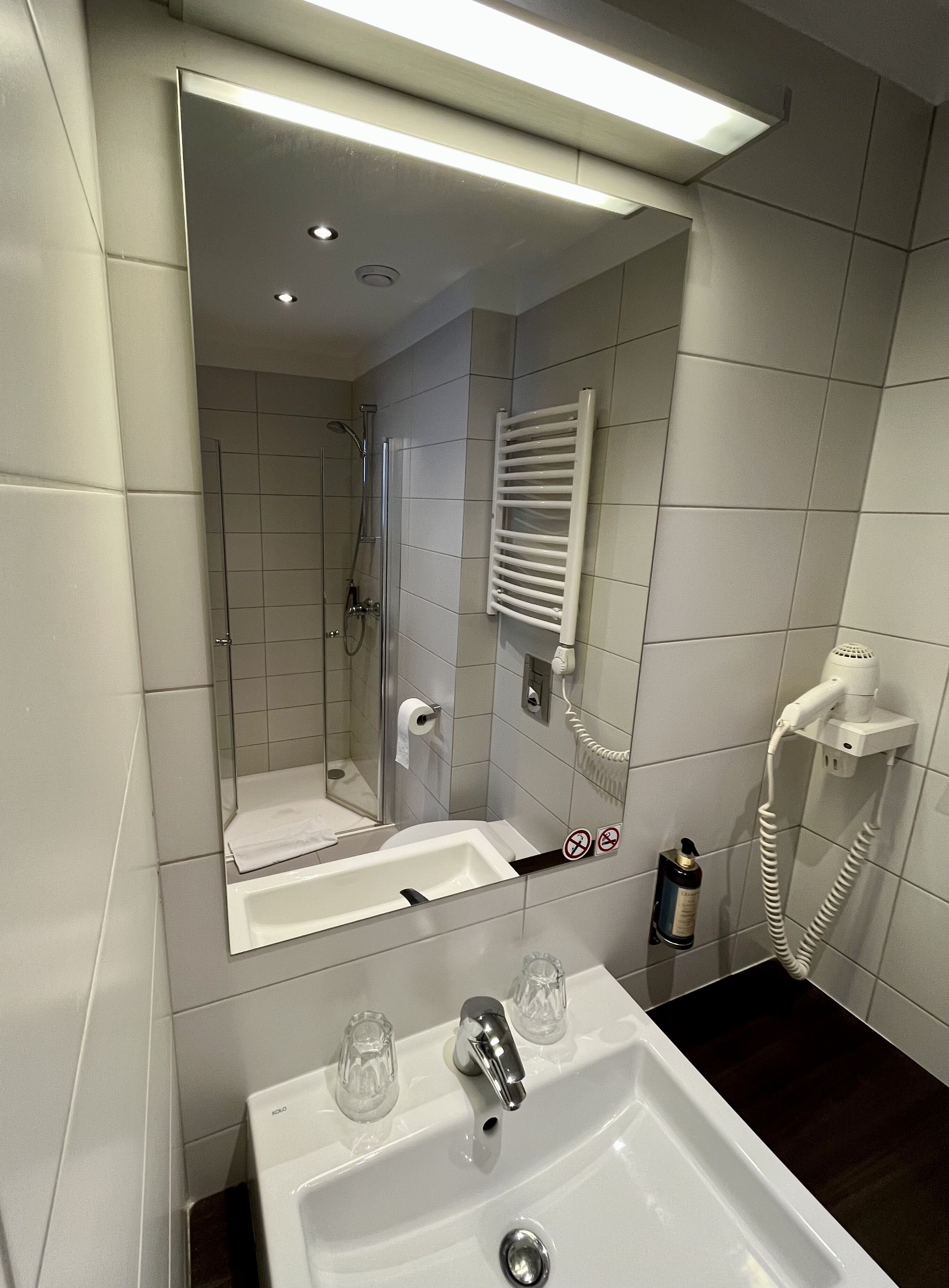 Ein modernes Badezimmer mit großem Spiegel, Waschbecken, Dusche und Handtuchhalter.