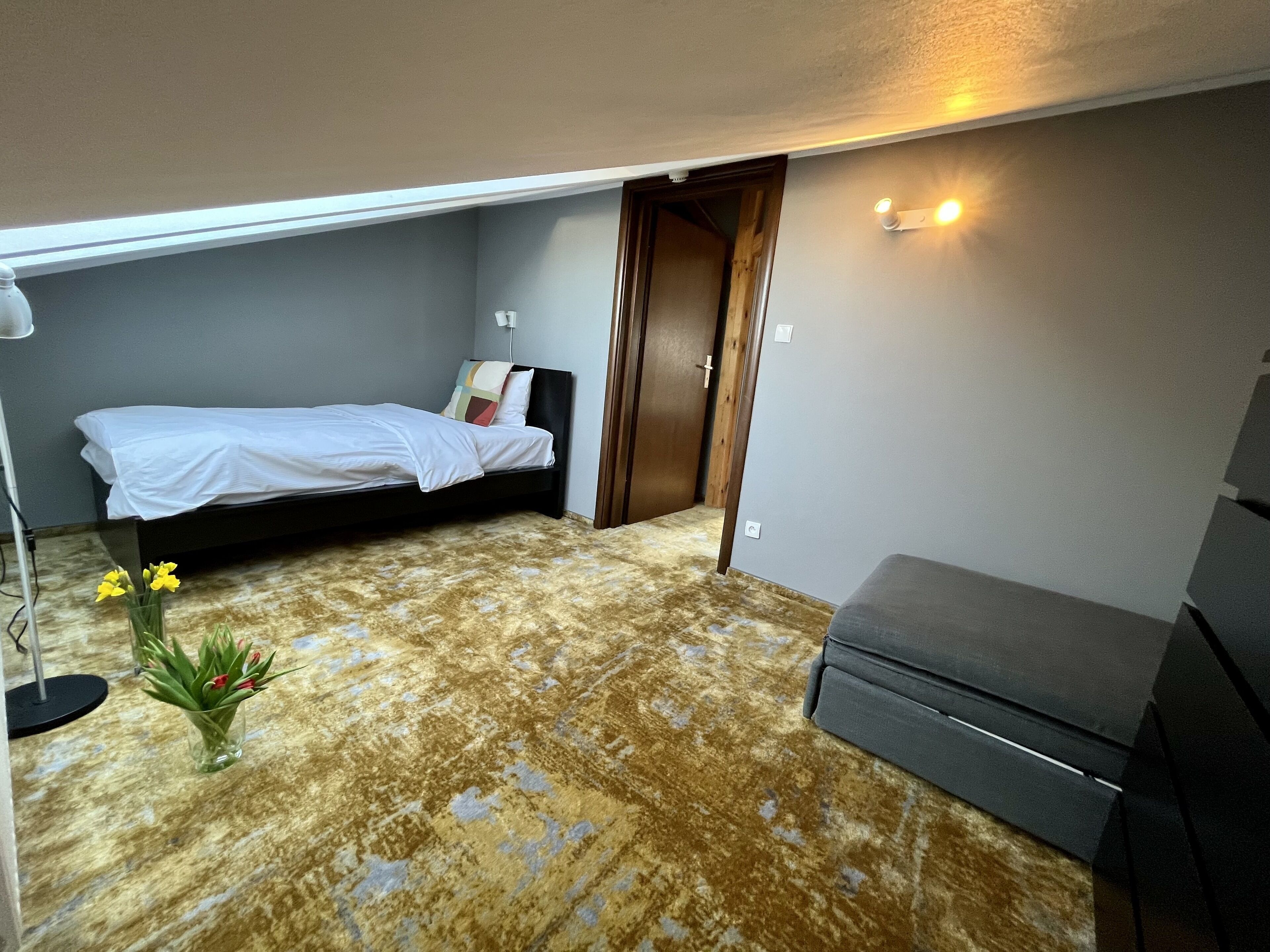A small, compact room with a bed, a sofa, and a small table with flowers.