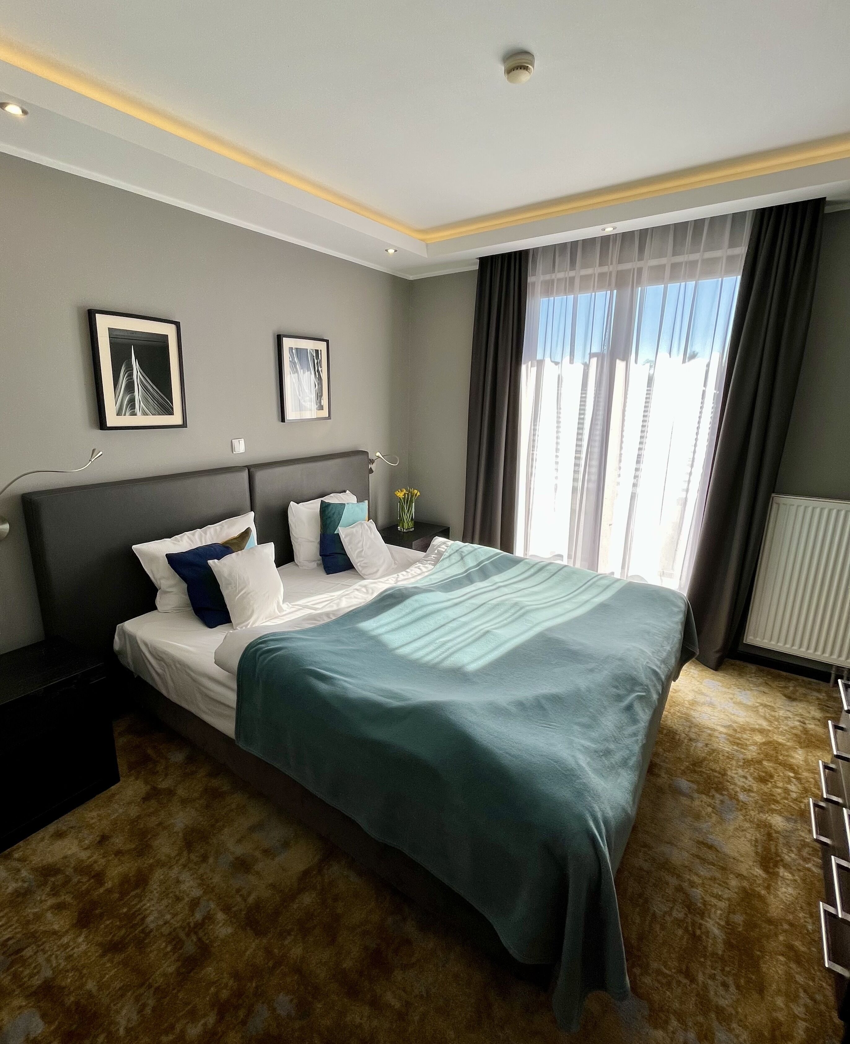 Ein modernes Hotelzimmer mit einem großen Bett, einem Nachttisch, einer Wandlampe und zwei gerahmten Bildern.