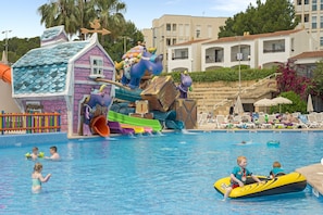 A swimming pool with a water slide, lounge chairs, and a building with a colorful facade. - FERGUS Club Europa (Calvia)