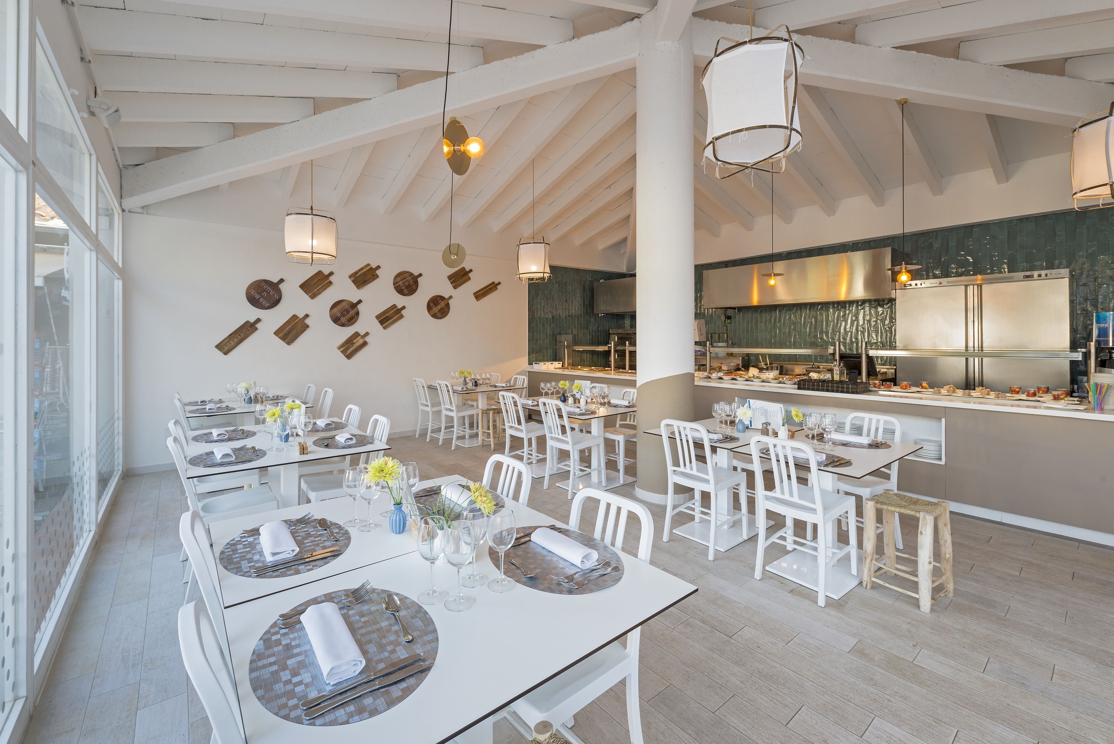 A spacious dining area with white tables and chairs, a kitchen in the background, and decorative wall art.