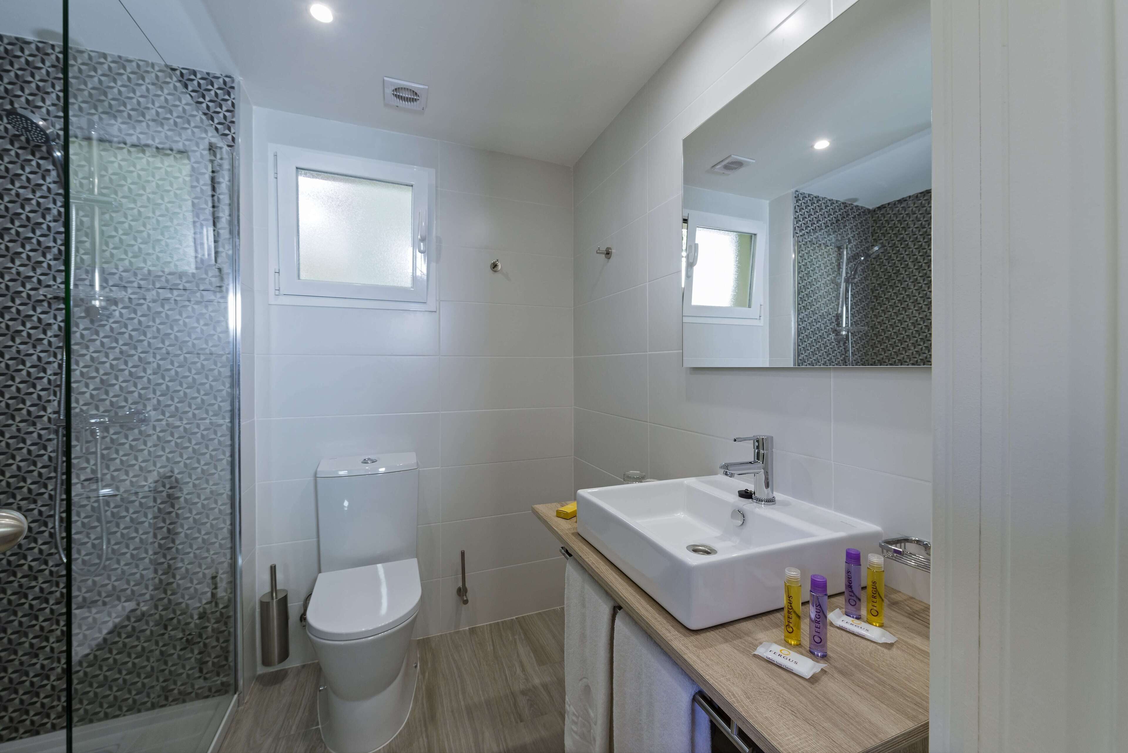Un baño moderno con ducha acristalada, inodoro y lavamanos con artículos de aseo.