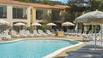 Uma área de piscina com espreguiçadeiras e guarda-sóis, um telhado telhado e um edifício com varandas.