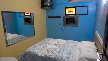 Quarto de hotel com cama, mesa de cabeceira, espelho, televisão fixada na parede e um letreiro com a inscrição 'LOVE STORY'.