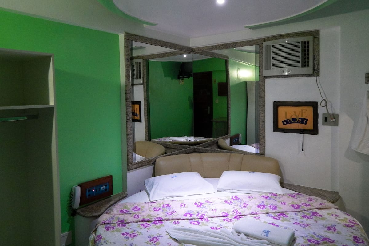 Une chambre à coucher avec un lit, un miroir, une table de chevet et un mur vert.