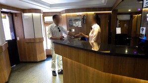 Un espace d’accueil d’hôtel comprenant un comptoir de réception en bois, un écran numérique et un panneau d’information fixé au mur.