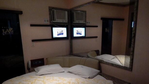 Une chambre d’hôtel avec un lit, deux téléviseurs fixés au mur, un miroir et une serviette sur le lit.