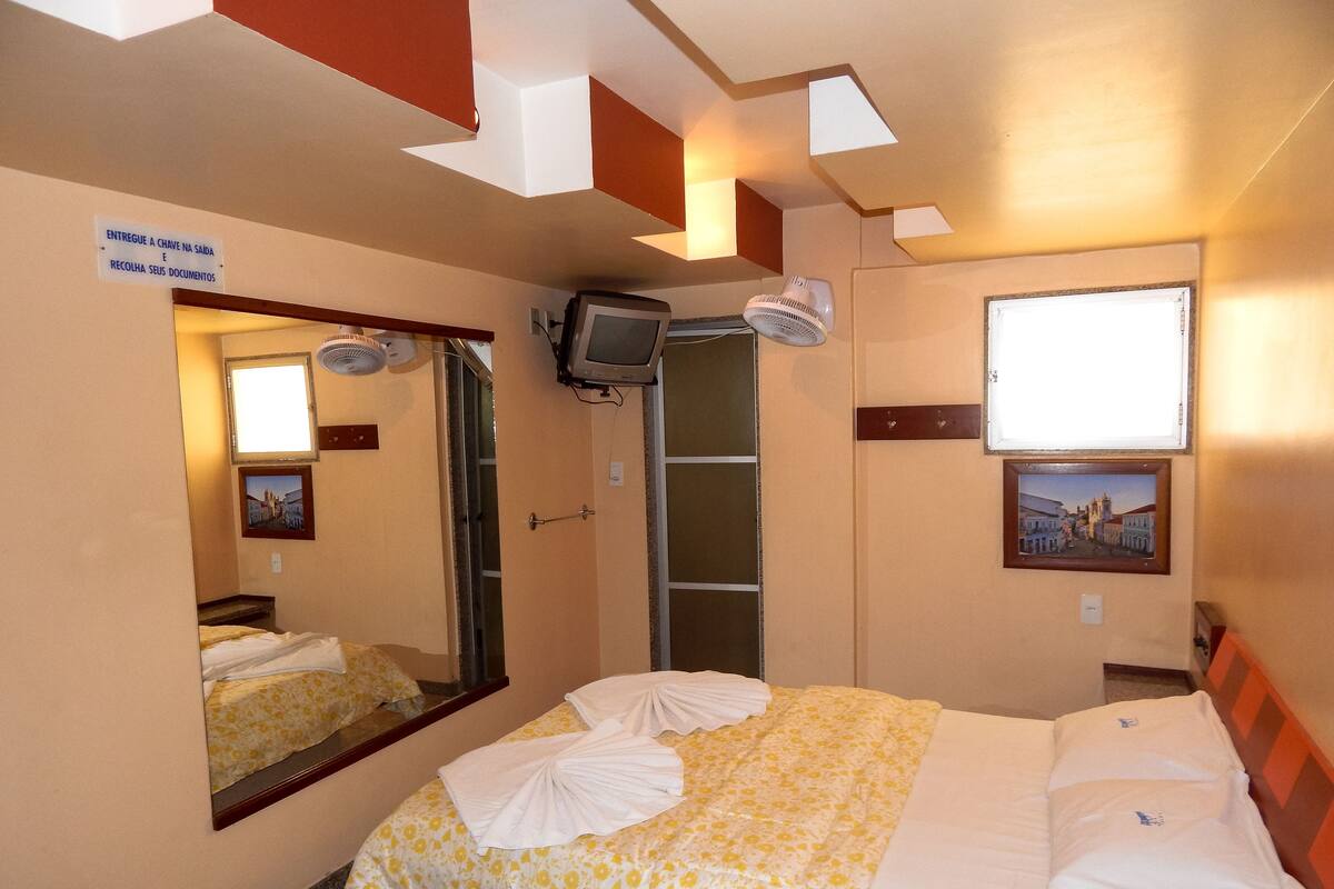 Une chambre d’hôtel avec un lit, un miroir, une télévision et une fenêtre.
