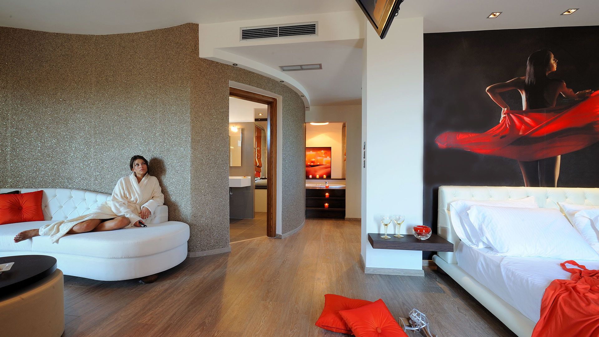 A modern hotel room with a white sofa, a bed, and a large painting of a woman in red.